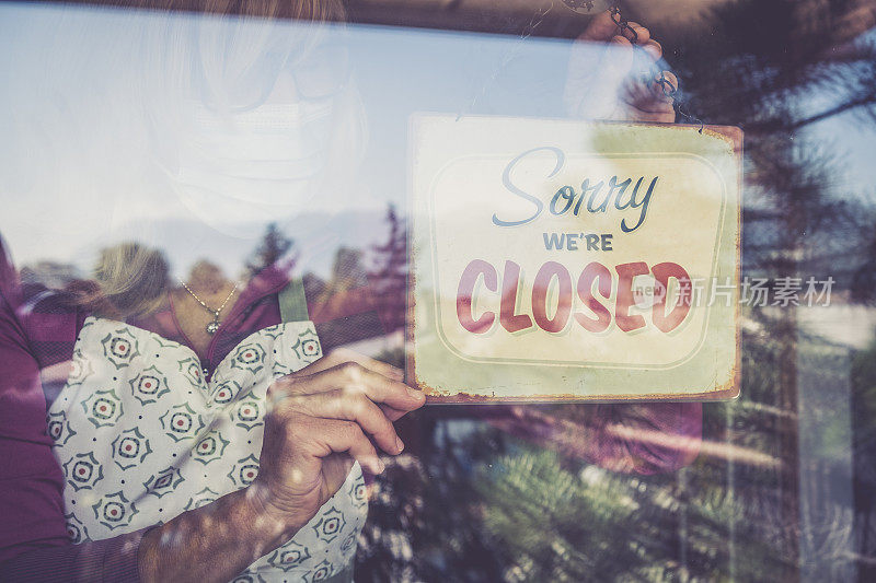 小企业关门了，女人在入口窗户上贴了"对不起，我们关门了"的牌子